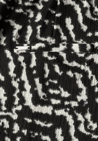 Tejido texturizado en blanco y negro con un patrón de estampado animal ondulado, con un bolsillo visible cosido y una etiqueta plateada que dice "Street One."