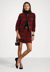 Raudona languota striukė ir sijonas, tekstūruotas audinys, auksiniai mygtukai, juodas viršus, juodas sagties diržas, juoda rankinė ir juodi aukštakulniai su logotipo detale.