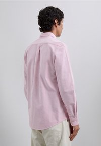 Let skjorte med krave, der har vertikale røde og hvide striber, lange ærmer, knappede manchetter og en buet nederste kant.