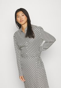 Black and white patterned dress with a scallop design, long sleeves, button-down front, and tie waist detail. Smooth fabric texture.