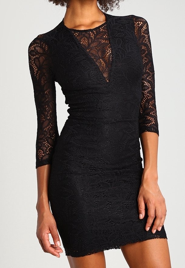 Femme portant une robe noire en dentelle ajustée avec des manches trois-quarts et un décolleté en V, montrant des motifs floraux en dentelle complexes.