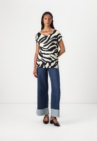 Top de manga corta a rayas negras y beige combinado con unos jeans de mezclilla azul de pierna ancha con un dobladillo en contraste y zapatos de tacón negro.