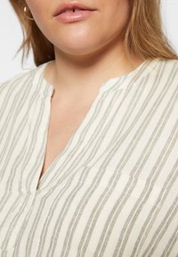 Blusa leve, riscada em creme e cinza. Apresenta um decote em V, mangas curtas e um corte relaxado com um tecido levemente texturizado.
