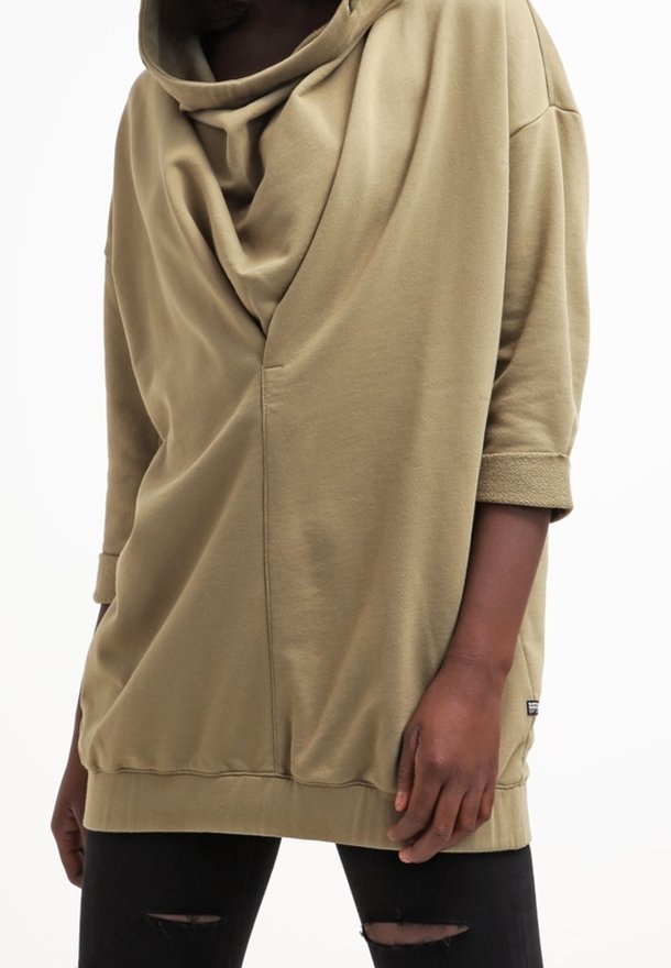 Sudadera oversize verde oliva con escote drapeado, mangas tres cuartos y detalles acanalados. Combinada con vaqueros negros rasgados.