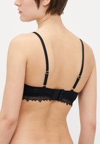 Bralette en dentelle noire avec des bretelles ajustables, un bord en dentelle festonné et une fermeture à crochet à l'arrière. Texture lisse.