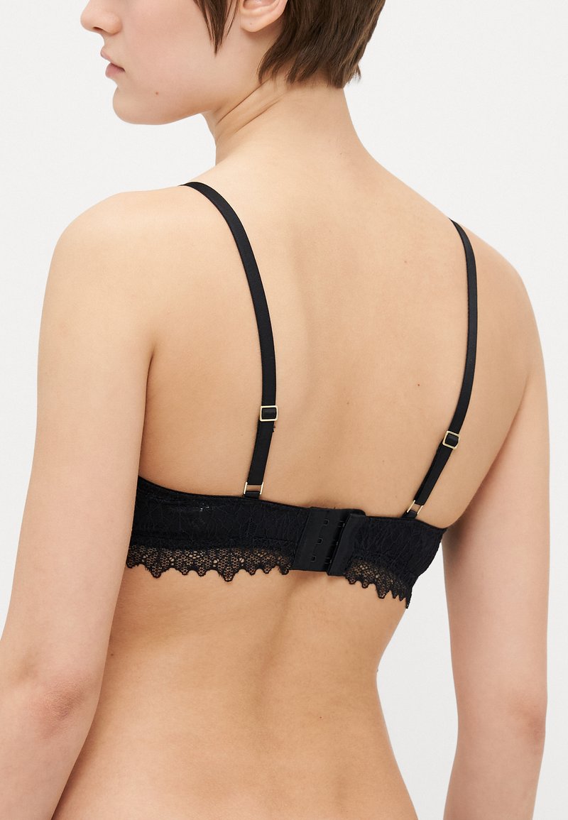 Bralette en dentelle noire avec des bretelles ajustables, un bord en dentelle festonné et une fermeture à crochet à l'arrière. Texture lisse.