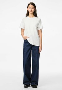 Vit t-shirt med kort ärm och rund halsringning, tillsammans med mörkblå vida denimbyxor med framfickor och avslappnad passform.