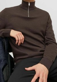 Brązowy sweter z zamkiem na szyi, z prążkowanymi mankietami i dołem. Miękka dzianina, z metalowym detalem zamka przy szyi. W połączeniu z ciemnymi spodniami.