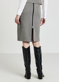 Jupe midi rayée grise avec une fermeture éclair au dos. Associée à de grandes bottes en cuir noir avec un accent en boucle et un petit talon.
