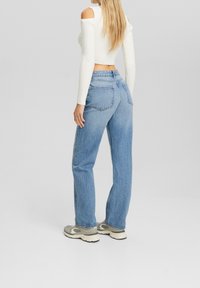 Jeans high-waisted di colore blu chiaro con una vestibilità rilassata, in tessuto denim e tasche posteriori, abbinati a un top bianco a costine cropped.