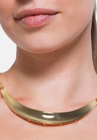 Collana metallica dorata con un design curvo e liscio. Presenta una finitura lucida e piccoli dettagli in metallo per un attacco sicuro.