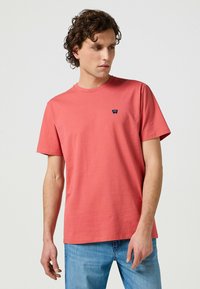 Korallfärgad kortärmad T-shirt i bomull med rund hals; har en liten blå logotyp på bröstet och en avslappnad passform.