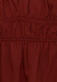 Červenohnědá tkanina se sbíranou texturou, vybavená elastickým pasem pro pružnost a pohodlí. Měkký, lehký materiál.