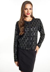 Cardigan negru cu model în carouri cu paiete, decolteu rotund, mâneci lungi și închidere cu nasturi. Purtați peste o fustă neagră.