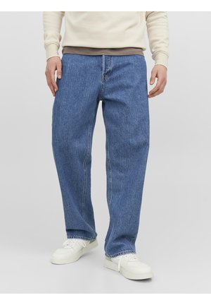 Vaqueros de mezclilla azul con un corte holgado, que cuentan con pasadores para cinturón, bolsillos frontales y una tela texturizada. Combinados con una blusa de capas en tonos beige y marrón.