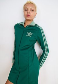 Roheline lukuga kleit pehmest kangast, millel on helesinine krae, kolm vertikaalset triipu varrukatel ja adidas logo rinnal.