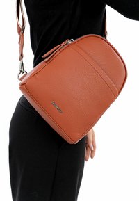 Bolso cruzado de cuero marrón con un acabado texturizado, forma redondeada, cierre de cremallera y una correa desmontable. Presenta un acento de marca.