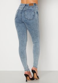 Jeans skinny in denim blu con vita alta, cinque tasche e leggera scoloritura. Abbinati a scarpe nere con tacco alto.