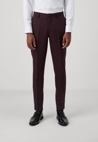 Burgundi színű, slim fit szabású, lapos elülső részű és sima textúrájú nadrág. Fekete, fényes cipővel és fehér, gombos inggel párosítva.