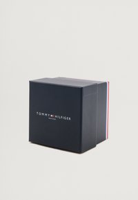 Fekete, matt felületű téglalap alakú doboz, fehér "TOMMY HILFIGER WATCHES" logóval és piros-kék díszcsíkokkal a szélein.