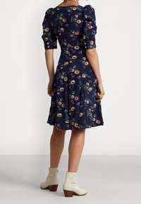 Vestido navy con flores, mangas cortas tipo globo, cintura ajustada y falda acampanada. Presenta un patrón de flores multicolores y acentos de botones. Botines blancos hasta el tobillo.