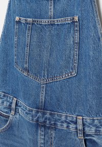 Blauwe denim overall met een achterzak, zichtbare stiksels en een tailleband met een contrasterende textuur. Eenvoudig en functioneel ontwerp.
