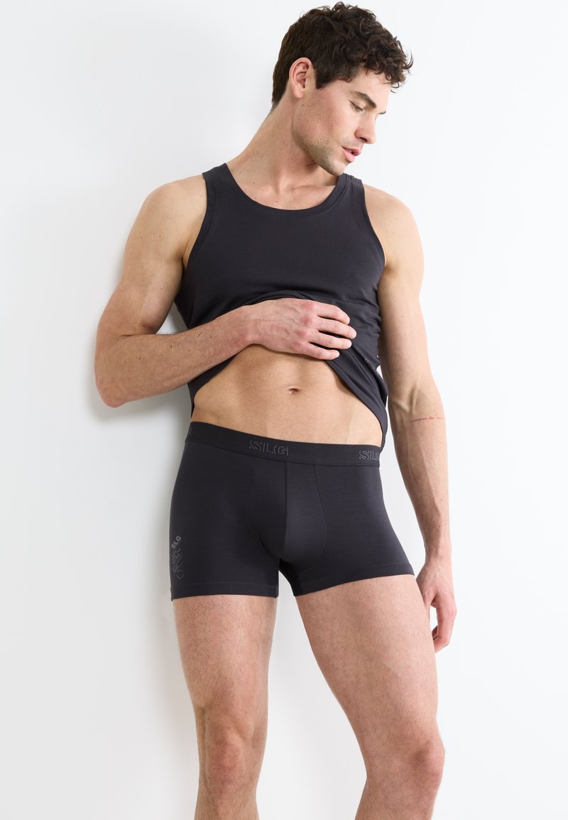 Canotta nera in cotone e pantaloni boxer, con una texture liscia, vita elastica e discreto logo. Design aderente, stile minimalista.