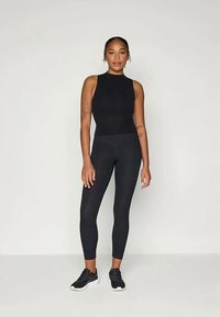 Completo sportivo nero composto da un top senza maniche e leggings a vita alta, realizzato in tessuto morbido ed elastico, abbinato a sneakers nere.