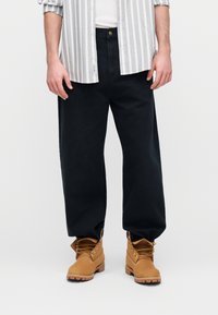 Σκούρο μπλε παντελόνι φαρδύ, σε συνδυασμό με λευκό και γκρι ριγέ πουκάμισο και ταμπά μποτάκια με κορδόνια, λαστιχένιες σόλες και μεταλλικά ρούχισμα.