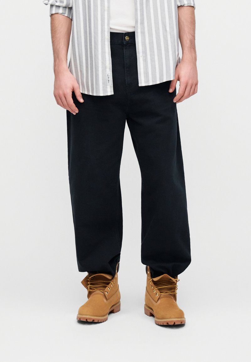 Mørkeblå bukser med vide ben kombineret med en hvid og grå stribet skjorte og brune snørestøvler med gummisåler og metalknapper.