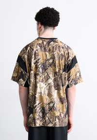 Kortærmet skjorte i et camouflage-mønster med nuancer af brunt og sort. Har en afslappet pasform og kontrasterende sorte sidelapper.