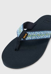Blå og gul mønstret stropp med svart gummisole flip-flop sandal. Har teksturert fotseng og Teva-logo på stroppen.