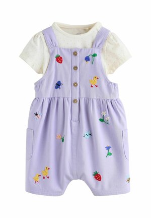 Lila Jumpsuit mit Knöpfen, bestickten Erdbeeren, Blumen und Tieren, getragen über einem cremefarbenen Kurzarmshirt mit Punkten.