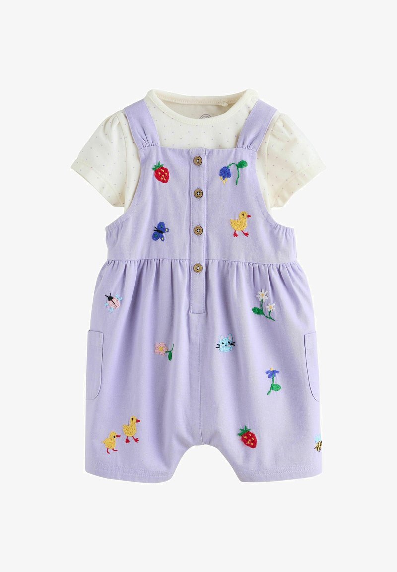 Levendulalila napozó gombokkal, hímzett eperrel, virágokkal, állatokkal, krémszínű pöttyös rövid ujjú ing fölött viselve.