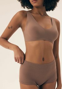 Jasnobrązowy bezprzewodowy biustonosz z szerokimi ramiączkami, o gładkiej teksturze. W połączeniu z dopasowanymi, prążkowanymi majtkami typu boyshort, oba w podobnym stonowanym odcieniu.