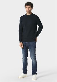 Maglione a costine in blu navy scuro con scollo a crew abbinato a jeans blu e sneakers bianche. La vestibilità è rilassata, mettendo in risalto il tessuto strutturato.