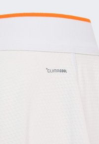 Biely textil s textúrovaným povrchom a pásom so zvýraznením v oranžovej farbe, s logom "CLIMACOOL" v sivej výšivke.