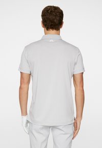 Light grey polo shirt made of smooth fabric, featuring a collar, short sleeves, and a small logo at the back neckline.