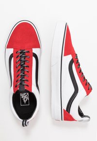 Baskets en toile rouge et blanche avec accents noirs, dotées de lacets ronds, d'un col matelassé et d'une semelle en caoutchouc blanche.