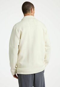 Witte fleece pullover met een kraag, voorzien van een gestructureerde afwerking, verlaagde schouders en een subtiele logo-details op de achterkant.
