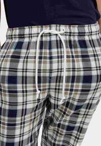 Rute pyjamasbukser med snor i taljen, lavet af blødt stof. Farverne inkluderer marineblå, hvid, grøn og brun med et ternet mønster.