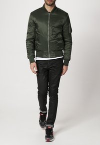 Veste bomber en satin vert foncé, avec une fermeture éclair à l'avant, des poignets côtelés et une poche latérale. Associée à un jean noir slim et des baskets.