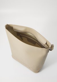 Borsa a spalla in pelle beige con una texture liscia, chiusura con zipper e logo impresso su un lato. L'interno include una tasca con zipper.