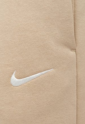 Tessuto beige con motivo lavorato a maglia testurizzato. Presenta un logo Nike ricamato bianco posizionato sul lato sinistro.