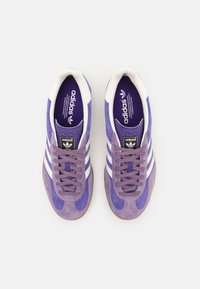 Zapatillas de ante púrpura con rayas blancas, cordones texturizados, plantillas en contraste y detalle en negro del logotipo en la lengüeta. Suela de goma.