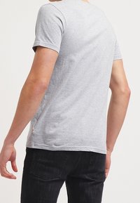 Camiseta de algodón gris con mangas cortas y cuello redondo, con una textura suave y un pequeño detalle de logo en el dobladillo.