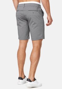 Grijze shorts met een gestructureerd patroon, voorzien van zijzakken en een met knoop sluitende achterzak, gedragen met witte sneakers.