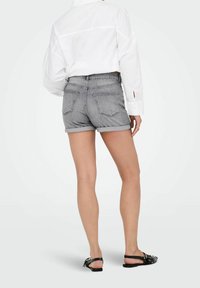 Szare dżinsowe szorty z podwiniętym dołem, tylnymi kieszeniami i średnim stanem, w zestawie z białą koszulą z długim rękawem i czarnymi sandałami.