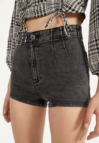 Černé džínové šortky s vysokým pasem byly nošeny se zkráceným, uvázaným dlouhým rukávem v kostkované potisku, který odhaluje břicho a část paží a rukou.