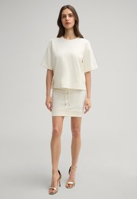 Hellbeige übergroßes T-Shirt mit abgesenkten Schultern und geradem Saum, kombiniert mit einem passenden, figurbetonten Minirock mit verstellbarem Kordelzug.